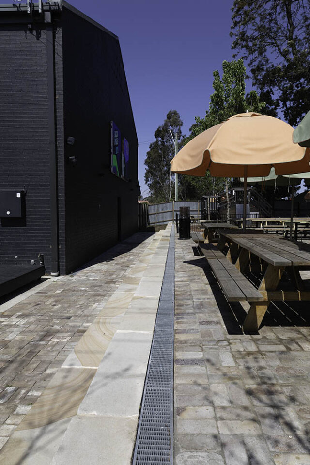 Beer garden on a sunny day. The ground is covered with sandstone and galvanised steel drainage is installed.