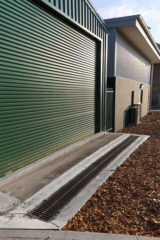 Cast iron drainage grate installed outside a green corrugated metal garage door