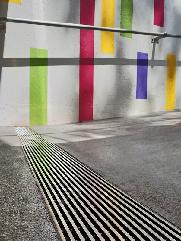 Stainless steel drainage grate is installed in front of a colourful mural